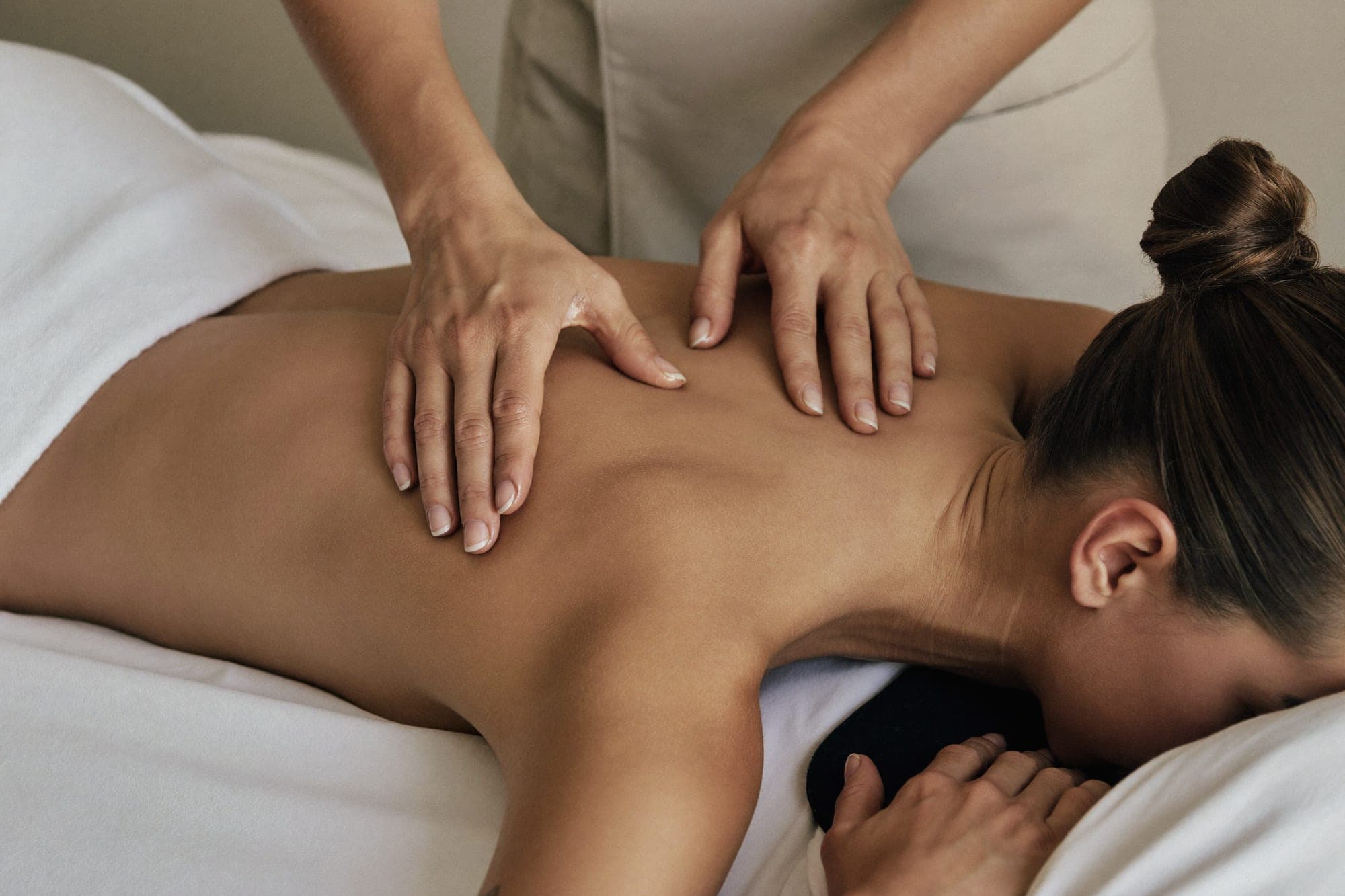 Therapist’s hands working across a client’s shoulders on the couch