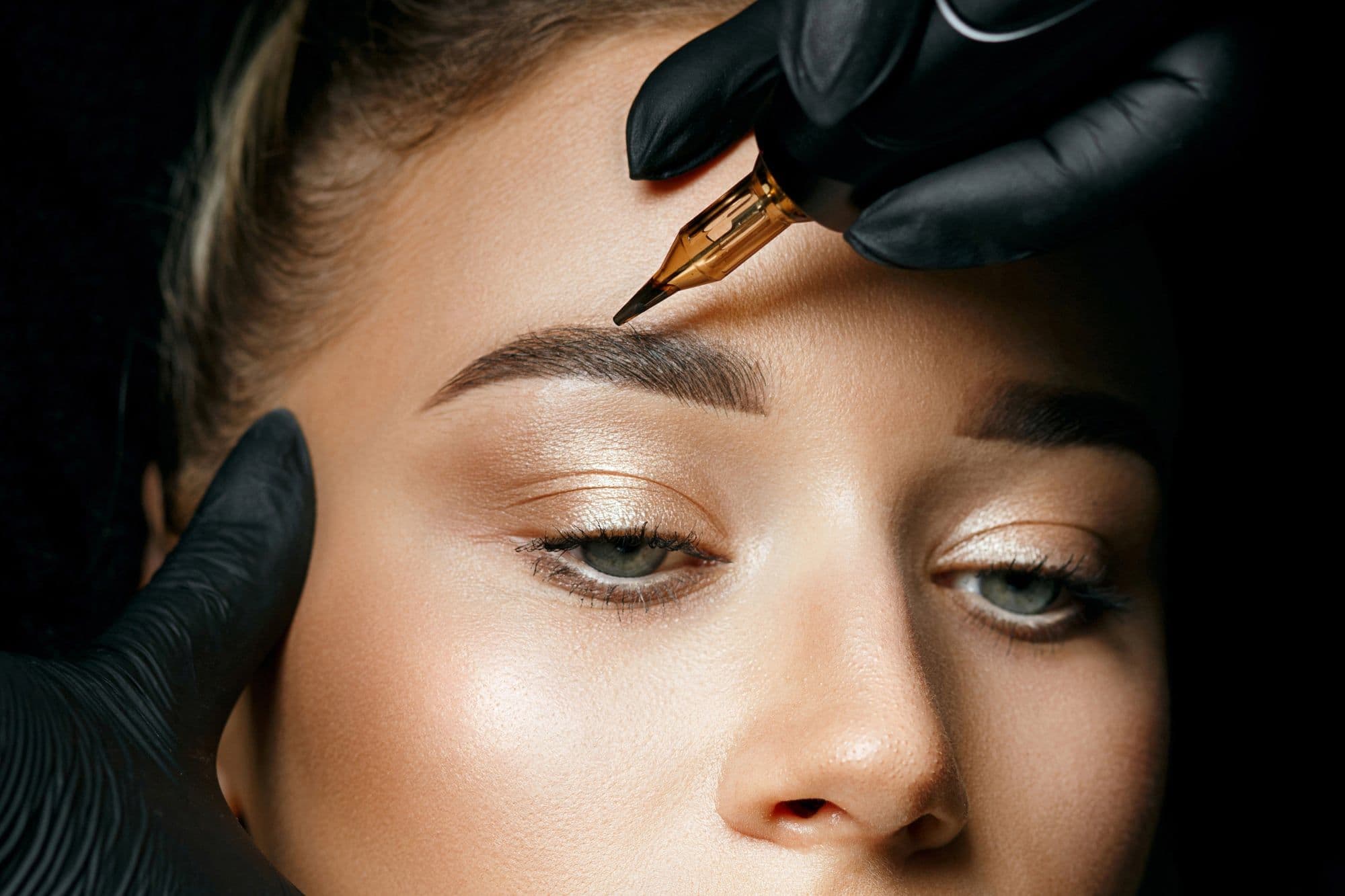 Brow being drawn with a fine pen, the artist’s gloved hand steadying the face