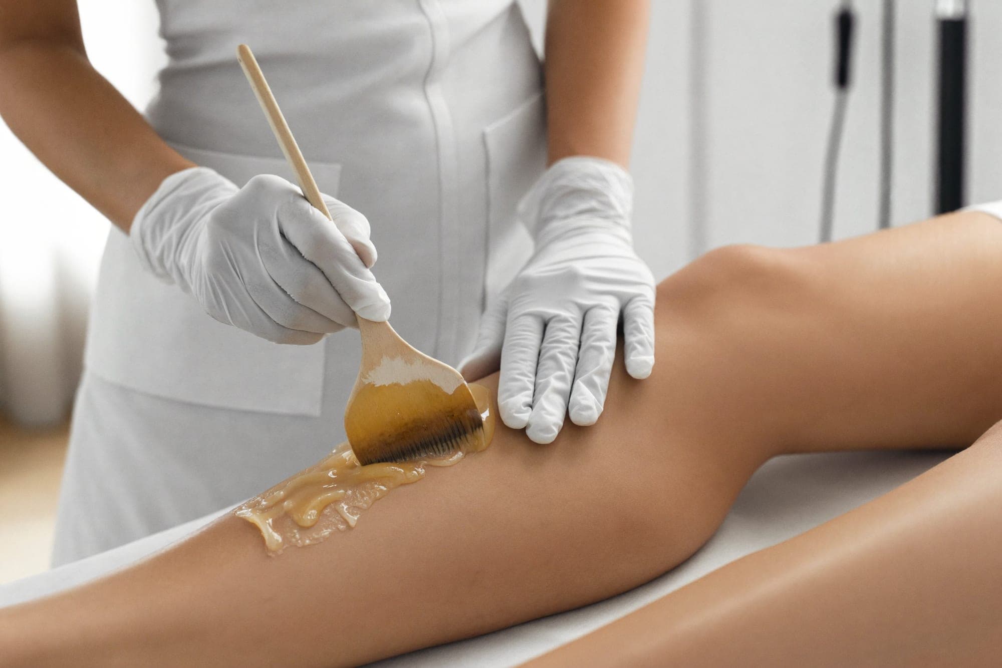 Warm wax being spread along a client’s lower leg with a spatula